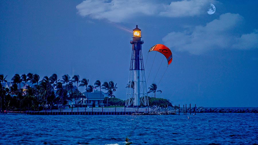 Lighthouse at dusk with a kite surfer over the water