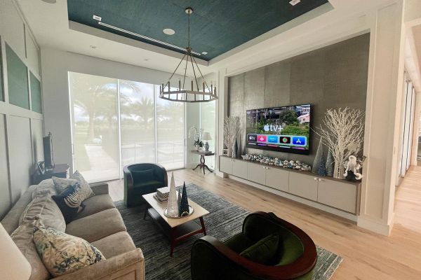 Neutral colored living room with tv in wall and candle type lighting hanging from the ceiling and closed shades