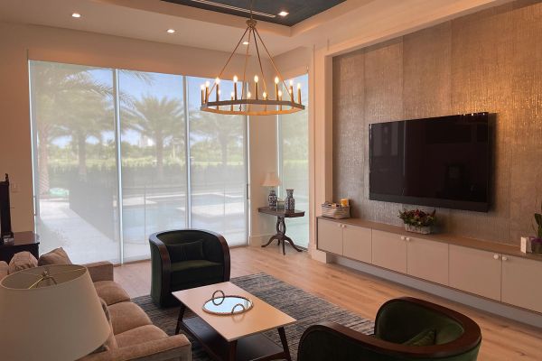 Neutral colored living room with tv in wall and candle type lighting hanging from the ceiling