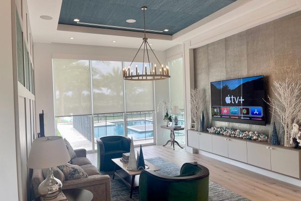 Neutral colored living room with tv in wall and candle type lighting hanging from the ceiling and halfway open shades